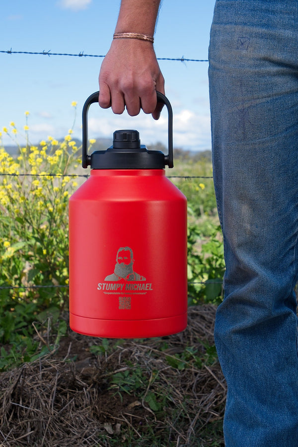 Red Stumptown coffee container held by a person outdoors with greenery and blue sky in the background