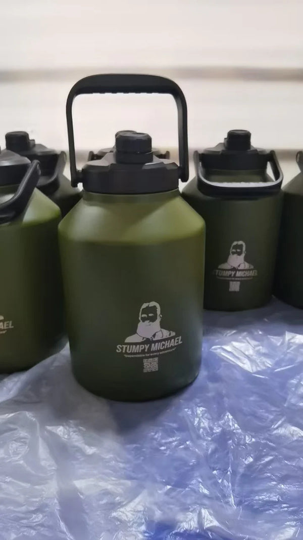 A green 6 litre stainless steel water bottle with a black lid and carrying handle, branded with 'Stumpy Michael'.