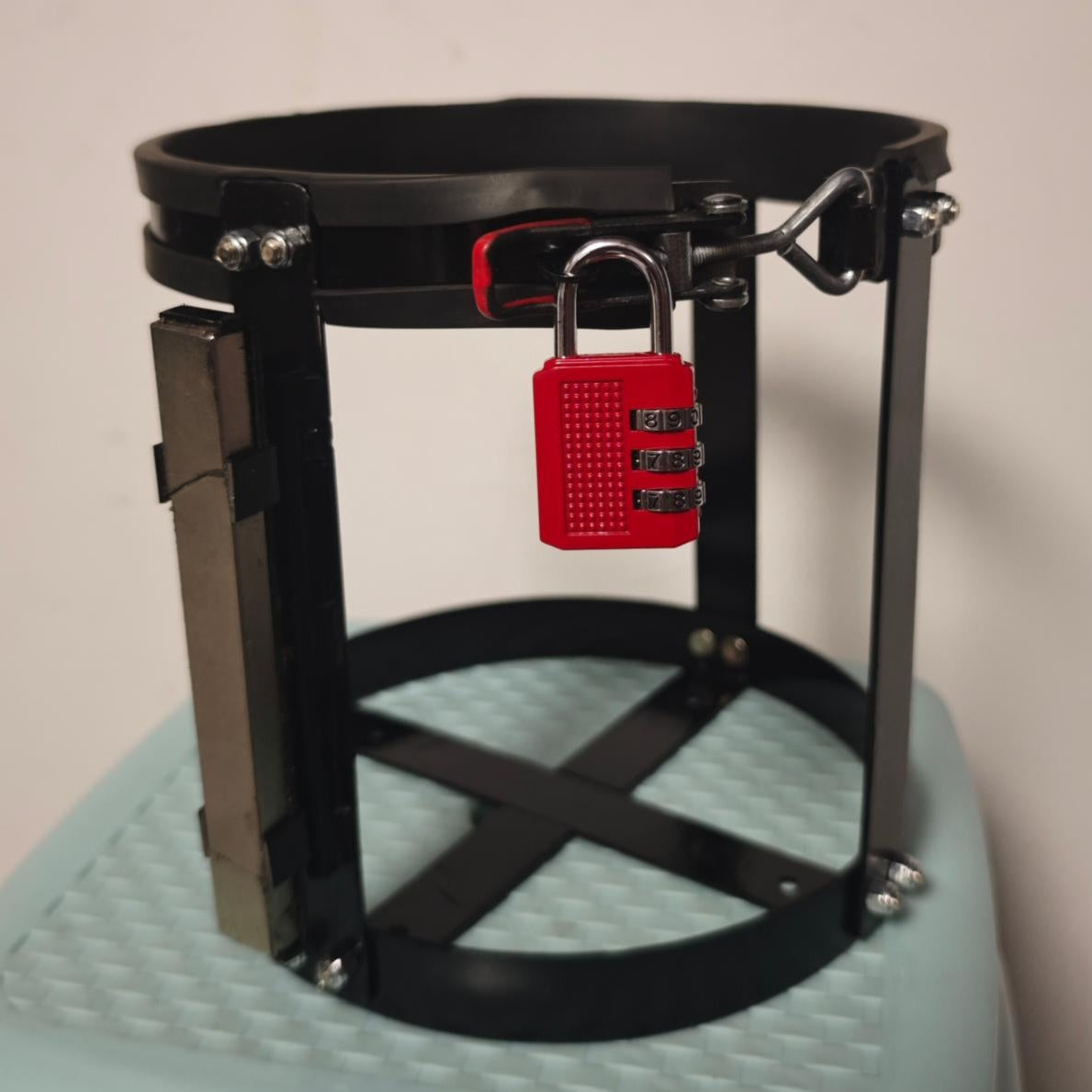 Black metal cage with a red lock on a light blue stool against a beige wall.