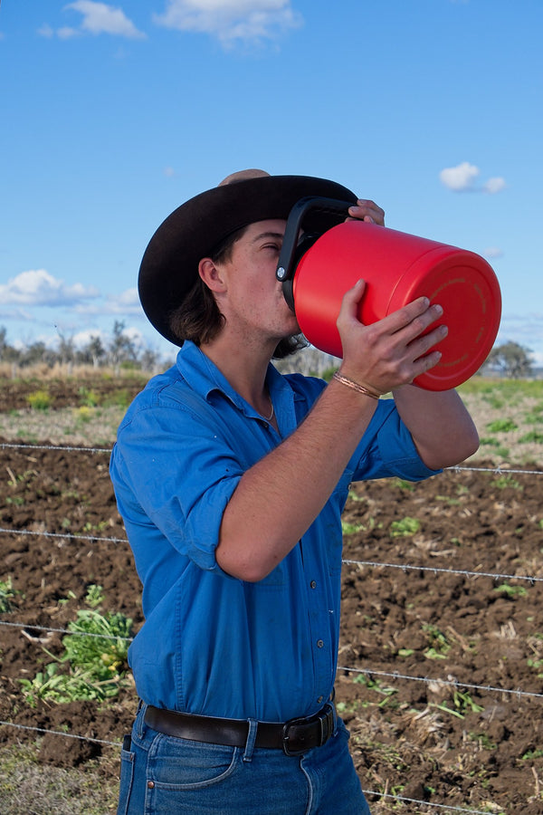 Person in a blue shirt and cowboy hat drinking from a red container