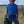 Man in a blue shirt and cowboy hat holding a green container in an open field.