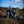 Man sitting on a hillside with a green container, under a blue sky with clouds.